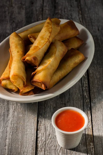 Homemade spring rolls with chinese sweet and sour sauce. In a white plate on a wooden background