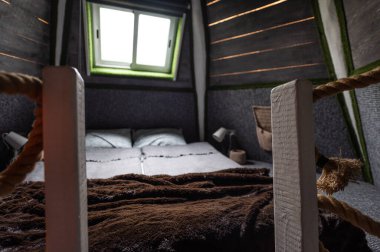 Curved woven hemp rope as decoration and security element for the railing frame of the stairs to the second bedroom floor in wooden summer house. End brush of a rope connected to wooden bars. Bed on a second floor in bungalow cabin.