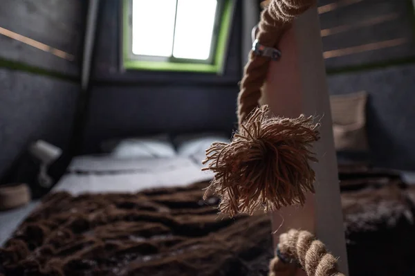 Curved woven hemp rope as decoration and security element for the railing frame of the stairs to the second bedroom floor in wooden summer house. End brush of a rope connected to wooden bars. Bed on a second floor in bungalow cabin.