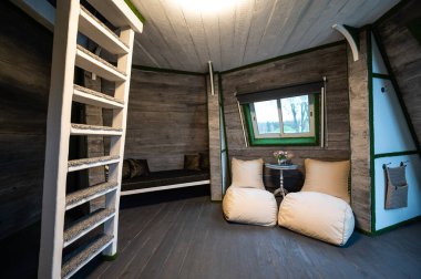 Wooden interior design. Living room of summer house. Pyramid shape bungalow from inside. Floor, walls, ceilings, stairs made of wood. Gray white colors of country interior. Beanbags in the niche