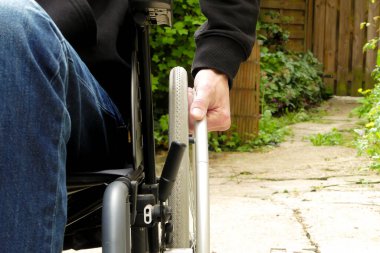 Tekerlekli sandalyedeki engelli biri. Bitki örtüsü olan bir sokakta hareket kabiliyeti düşük bir adam..