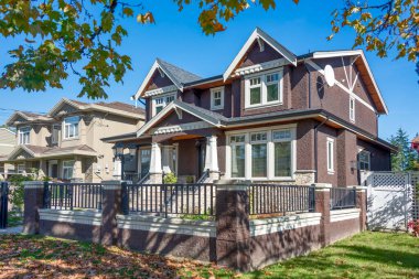 Önünde mavi gökyüzü arka planında parmaklıklar ve parmaklıklar olan lüks bir ev. Taştan çitlerin arkasında büyük ön bahçesi olan lüks bir aile evi.