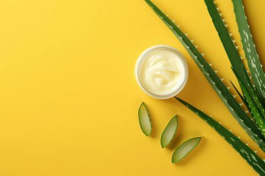 Kremalı kavanoz ve sarı arka planda aloe yaprakları. Düz yatıyordu. Kozmetik için boş reklam afişi şablonu.
