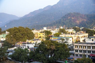 Rishikesh, Hindistan 6 Aralık 2024: Triveni Ghaat yakınlarındaki Rishikesh kasabasının akşam güneşiyle aydınlatılmış ve Shivalik dağları tarafından çerçevelenmiş altın saat manzarası.