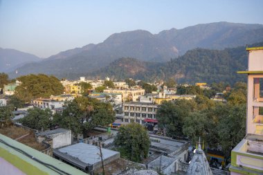 Rishikesh, Hindistan 6 Aralık 2024: Triveni Ghaat ve Shivalik Himalaya dağlarının arka planında yer aldığı yukarıdan Rishikesh kasabasının panoramik manzarası.