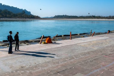 Rishikesh, Hindistan, 06 Aralık 2024: Triveni Ghaat 'ta gezinen turistleri çeken bir sahne, bir Yogi azizi Rishikesh' teki nehir kıyısında namaz kılarken.