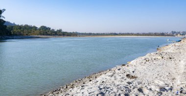 Triveni Ghaat 'ta akan kutsal Ganj Nehri' nin huzurlu bir manzarası, berrak mavi suları ve her iki tarafında da görünen nehir kıyılarıyla..