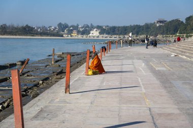 Rishikesh, Hindistan 6 Aralık 2024: Safran cübbe giymiş ruhani bir figür Rishikesh 'teki Triveni Ghaat' ın Ganj Nehri kıyısında oturuyor.
