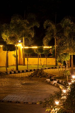 Aydınlatılmış arka bahçe sarı ışıklarla süslenerek sıcak bir parıltı yaratıyor. Aydınlatılmış bitkiler ve ağaçlar uzayın büyüleyici atmosferini arttırır..