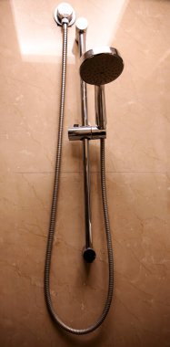 Modern bir duş başlığı banyoda kahverengi-turuncu duvar fayanslarının yanında yer alır. Basit, şık tasarım temiz ve taze bir atmosferi teşvik eder..