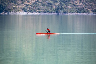 In calm water, a man rows a kayaking boat with an oar at Tehri Lake. The tranquility of the surroundings complements the activity, making it a serene experience. clipart