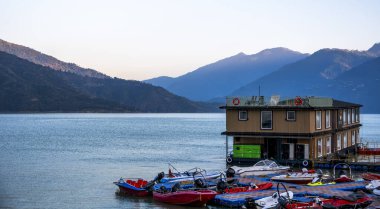 Tehri Lake, India  December 06, 2024: A floating hotel can be seen in Tehri Lake with small boats nearby. The majestic mountains in the background enhance the picturesque scenery of the location. clipart