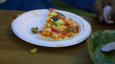 Beyaz bir tabak çeşitli sebzelerle kaplı bir dilim pizzanın yanında bir turta tutar. Sunum iştah açıcı ve renkli..