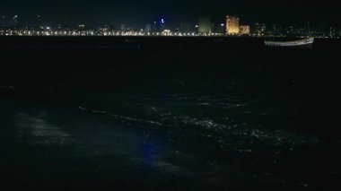 Mumbai, Hindistan 22 Şubat 2025: Deniz kıyısında bir tekne yüzüyor, yüksek binaların gece parladığı ve dalgaların sahile vurduğu yerde..