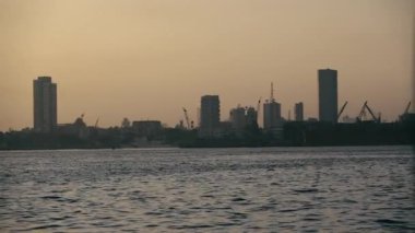 Sahne, akşamları deniz kıyısı boyunca uzanan limanları ve ufuk çizgisini gösteriyor. Güneş arkada batıyor ve muhteşem bir manzara yaratıyor..