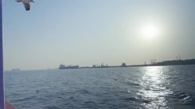 Bir teknenin manzarası deniz yolculuğunu gösteriyor. Binaların görüldüğü kıyıya yaklaşıyor..