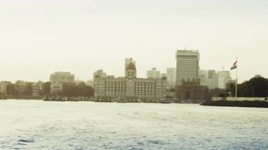 Mumbai şehrinin ufuk çizgisi denizin ötesinde, ihtişamını gözler önüne seriyor. Gemiler ve tekneler denizde özgürce dolaşarak hareketli aktiviteyi tamamlıyorlar. Güneş şehrin arkasında parlıyor, üzerinde kuşlar uçuşuyor..