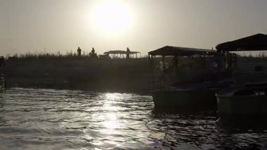 Teknelerin karanlık silueti Yamuna 'nın nehir kıyısındaki insanlarla çelişiyor. Sahne, suyun kenarında hem hareketsizliği hem de hareketsizliği yakalar..