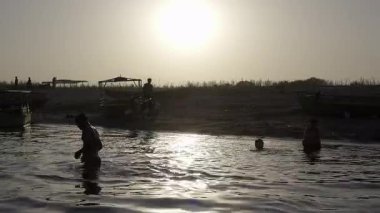 Vrindavan, Mathura, Hindistan 30 Mart 2025: İnsanlar arka planda nehir kıyılarının karanlık silueti ile Yamuna Nehri 'nde yıkanırken görülebilir. Sudaki tekneler ve kıyılardaki motorlar ortamı güzelleştiriyor..