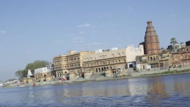 Yamuna Nehri 'ndeki Keshi Ghat' in uzun bir görüntüsünde çeşitli tapınaklar, kenarda yürüyen insanlar ve sudaki yansımalar bölgenin cazibesini ön plana çıkarıyor..
