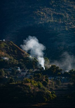 Dağlarda yuva yapmış, çok katmanlı zirveler ve derin yamaçlarla çevrili kasabalardan beyaz duman yükseliyor. Sahne, doğanın güzelliğini yakalar..