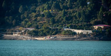 Tihri, Hindistan, 08 Aralık 2025: Göl kıyısındaki bir tatil beldesinde aşağıda park etmiş arabalar ve kamyonlar güzel mavi bir göle erişim sağlamaktadır. Mekan ziyaretçiler için mükemmel bir kaçış yolu sunuyor..