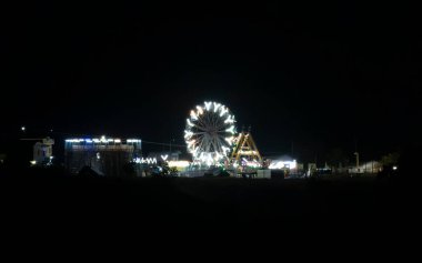 Aydınlatılmış bir atlı karınca salıncağı panayırda duruyor, ölüm kuyusu ve Columbus salıncağının yanında. Canlı karnaval ilgi çekici bir gece sahnesi yaratıyor..