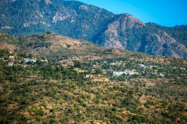 Sarı güneş ışığı yeşil kaplı dağları yıkarken, küçük kasabalar uzakta belirir. Sahne sıcaklık ve dinginlik yayar, keşifleri davet eder..
