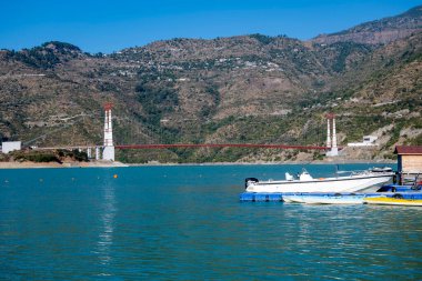 Tihri, Hindistan, 08 Aralık 2025: Hız tekneleri yakınlarda demirli iken, diğer tarafta bir köprü görülebilir. Sahne, su ve altyapı arasındaki dinamik ilişkiyi yakalıyor..