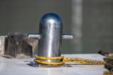 İp, bir kordona bağlanır ve bağlama teknikleri gösterilir. Limandaki metalik dalgalanma yatların ve teknelerin güvence altına alınması için gereklidir..