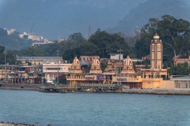 Rishikesh, Hindistan 08 Aralık 2024: Nehrin karşısındaki Parmarth Ashram 'ın uzun bir görüntüsü çevredeki tapınakları vurguluyor. Bölge ruhani ve huzurlu bir ortam yayıyor..