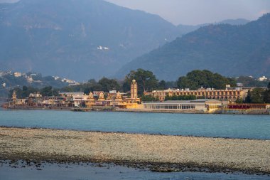Rishikesh, Hindistan, 08 Aralık 2024: Ganj Nehri 'nin karşısında yer alan Parmarth Ashram' ın uzun bir görüntüsü sergilenmektedir. Huzurlu manzara ruhani bir atmosfer sağlıyor..