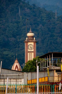 Rishikesh, Hindistan, 08 Aralık 2024: Rishikesh 'te yanında bir tapınak bulunan bir saat kulesi bulunmaktadır. Bu kombinasyon bölgenin kültürel ve tarihi önemini vurgular..