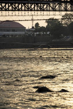 Rishikesh, Hindistan, 08 Aralık 2024: Nehrin karşısında bir otel kompleksi bulunuyor, yanında da bir köprü var. Bu ayar çarpıcı görüntüler ve bölgeye uygun erişim imkanı sunuyor.