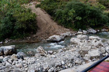 Kayaların arasından akan küçük bir nehir kaynağı ve yakınındaki enkaz yığınları. Bu doğal ortam dinamik ve huzurlu bir ortam yaratır..