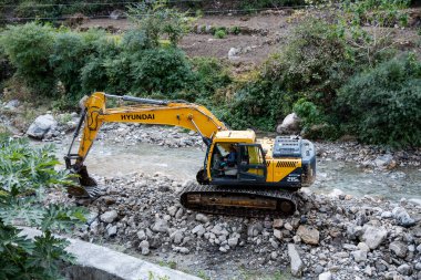Tihri, Hindistan, 08 Aralık 2024: İzlenen büyük bir kazıcı nehir yatağından kayaları ve enkazı kaldırmakla meşgul. Bu görev temiz bir su geçidi sağlamak için gereklidir..