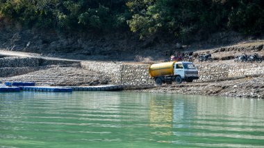 Tihri, Hindistan, 08 Aralık 2024: Gölün üzerinde park edilmiş bir su tankeri kamyonu bulunuyor. Bu pratik araç çevredeki toplulukların ve ziyaretçilerin ihtiyaçlarını karşılıyor..