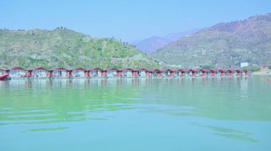 Tehri, Hindistan - 08 Ocak 2025: Göldeki yüzen kulübelerin dairesel manzarası büyük dağları ve kulübelerin arkasındaki köprüyü gösteriyor. Kompozisyon resim gibi bir manzara yaratıyor..