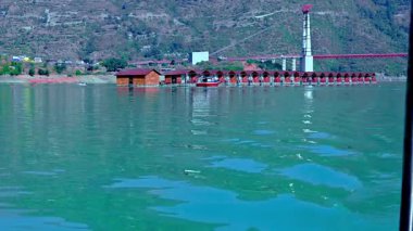 Tehri, Hindistan - 08 Ocak 2025: Göldeki yüzen kulübelerin dairesel manzarası büyük dağlar ve arkasında bir köprü sunuyor. Gidiş manzarası çevrenin güzelliğini vurguluyor..
