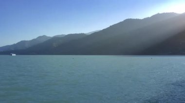 Güneş ışınları, su dalgalarının, yüzen bir otelin ve çarpıcı mavi göldeki dağların zamanlamasını aydınlatır..