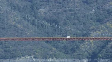 Dinamik bir manzara, köprünün üzerinden akan bir nehri ve manzaraya dağları ekleyen trafiği yakalar..
