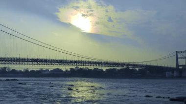 Büyüleyici bir sahne, bulutlu bir gökyüzünün altındaki köprüyü geçen insanları gösteriyor. Deniz mavisi ve turuncu renkler eşsiz bir atmosfer yaratıyor..