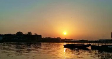 Günbatımı, Mathura kıyısındaki evlerin arkasındaki Yamuna Nehri 'ni aydınlatır. Gemiler suya yansıyan yansımalarla kenetlenir..