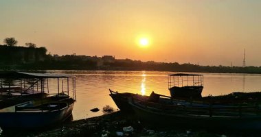 Mathura 'da günbatımının büyüleyici bir akşam manzarası Yamuna Nehri' ni vurguluyor. Tekneler kenetlenmiş ve yansımaları suda dans ediyor..