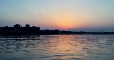 Nehrin manzarası Mathura 'da gün batımını gösteriyor. Evlerin arkasında, huzurlu bir akşam ortamı yaratıyor..
