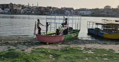 Mathura, Hindistan - 18 Mayıs 2025: Çocuklar Yamuna Nehri kıyısında bir teknede oynarken, yakınlardaki çöpler nehir kirliliğinin devam eden sorununu vurguluyor.