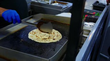 Düz ekmek, spatula kullanılarak sıcak bir tabakta pişiriliyor. Bu da yemek hazırlamada kullanılan yaygın bir pişirme tekniğini gösteriyor..