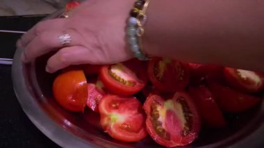 Tepside taze kesilmiş kırmızı domates parçalarını bir kadın daha fazla doğrarken, bir tepeden çekimde bir tepsi daha fazla kırmızı domates bulunur..