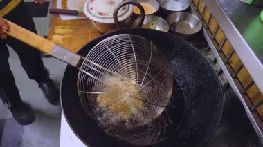 Yukardan aşağıya bakan bir manzara, anneleri kızgın bir yağ tenceresinde kızarırken yakar. Pişirme sürecini ve lezzetini gösterir..