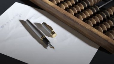 Klasik ahşap abaküs, dolmakalem ve üzerine el yazısıyla hesaplamalar yapılmış beyaz kağıt. Bir hesaplama aracı kavramı, matematik, aritmetik, okul, eğitim, muhasebe.